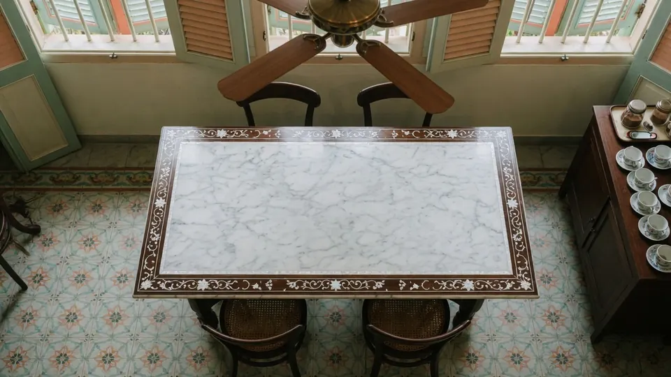 A marble-topped table on patterned floor tiles, under a ceiling fan.